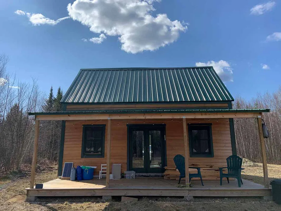 A compact steep-gable timber cabin with a covered porch in a woodland clearing.