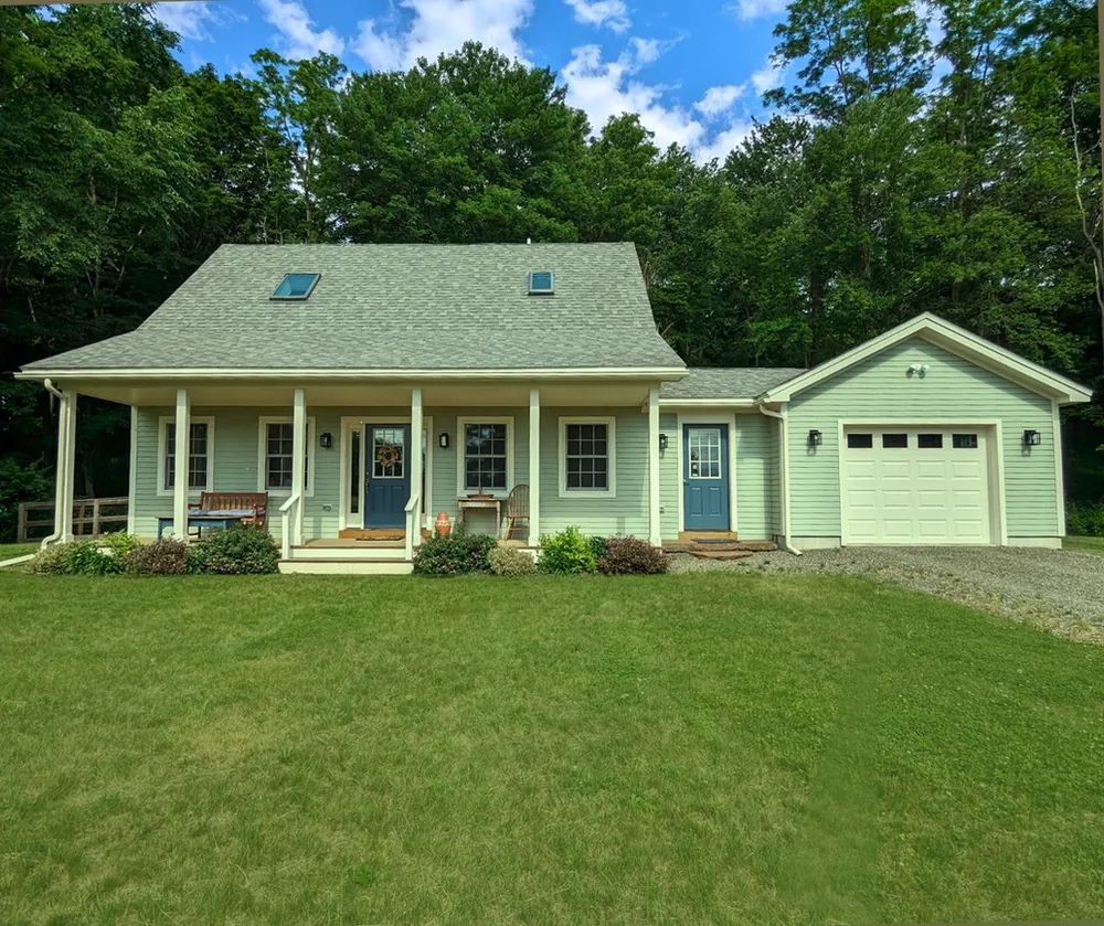 A pale green story-and-a-half side-gable home with symmetric windows and a full-width porch.